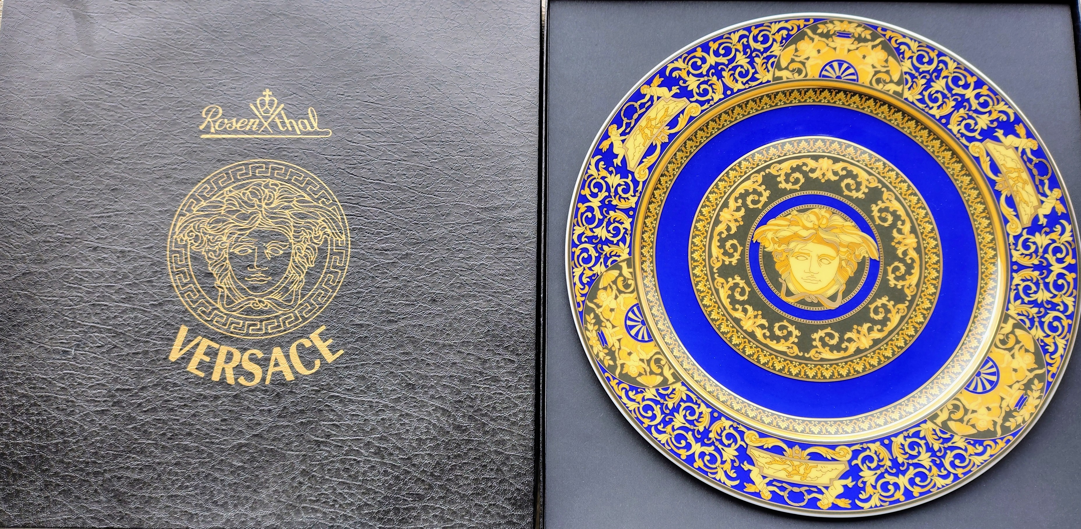 The opened black original box: on the left the lid with a golden Medusa head and the maker's lettering, on the right a round porcelain plate with a cobalt-blue rim, golden scrolls and cherubs, and a golden Medusa head in the centre